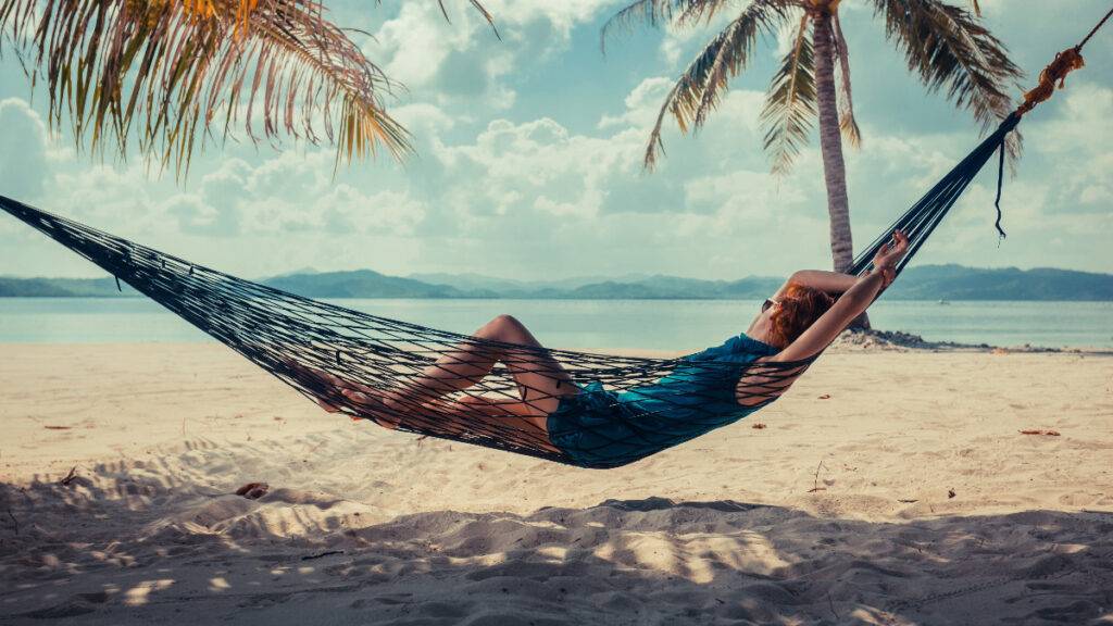 Woman relaxing in hammock on tropical beach to represent passive investing's hands-off approach